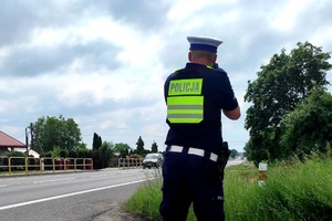Funkcjonariusz trzyma w ręku miernik prędkości skierowany w kierunku jezdni