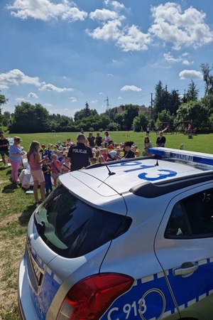 Radiowóz na pierwszym planie, w oddali policjant z dziećmi