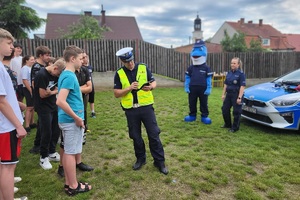 Policjant okazuje młodzieży zasadę działania sygnalizatorów radiowozu wypadkowego