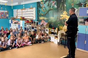 Przedszkolaki siedzą na dywanie, rozmawiają z policjantem