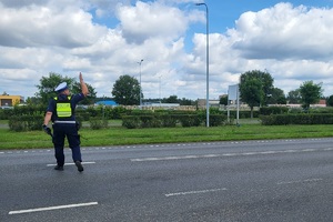 Policjant idzie jezdnią, unosi rękę aby zatrzymać pojazd