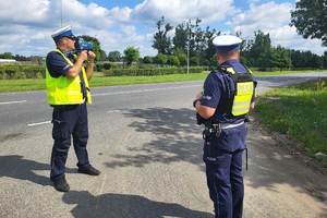 Policjanci stoją przy drodze, jeden z nich mierzy prędkość pojazdów