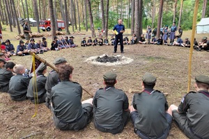 Harcerze siedzą w kółku, słuchają policjata