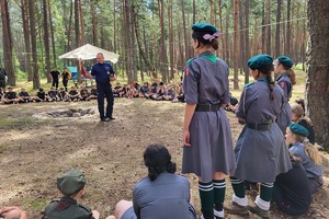 Harcerki stoją w kółku, słuchają policjata