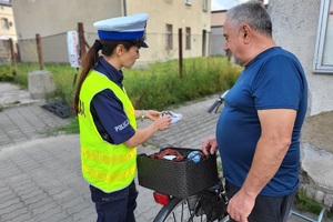 Policjantka rozmawia z rowerzystą, wręcza mu oświetlenie do roweru