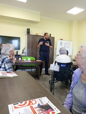 Policjant stoi przed rozmówcami, prowadzi spotkanie