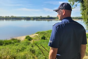 Policjant stoi  w rejonie brzegu rzeki