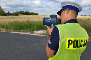 Policjant ruchu drogowego mierzy prędkość ręcznym miernikiem.