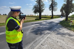 Policjantka za pomocą miernika kontroluje prędkość poruszających się drogą pojazdów