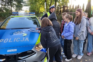 Policjant prowadzi przed szkołą rozmowę z uczniami