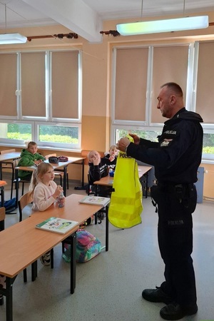 Policjant pokazuje dzieciom kamizelkę odblaskową