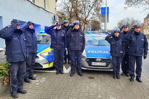 Policjanci stojący przy radiowozach oddają hołd