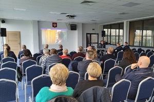 Seniorzy siedzący na widowni sali konferencyjnej