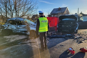 Policjant drogówki prowadzący czynności na miejscu wypadku, w tle uszkodzone pojazdy