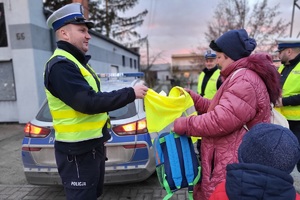 Policjant wręcza kobiecie kamizelkę odblaskową