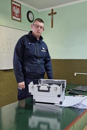 Policjant prezentuje walizkę edukacyjną