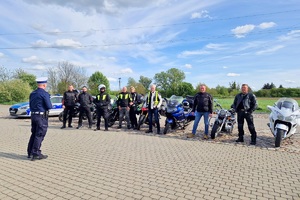 Policjanci ruchu drogowego rozmawiają z grupą motocyklistów i wręczają im szelki odblaskowe