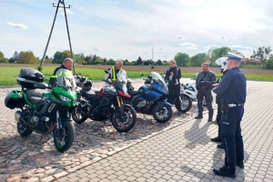 Policjanci ruchu drogowego rozmawiają z grupą motocyklistów i wręczają im szelki odblaskowe