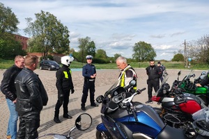 Policjanci ruchu drogowego rozmawiają z grupą motocyklistów i wręczają im szelki odblaskowe