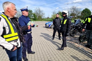 Policjanci ruchu drogowego rozmawiają z grupą motocyklistów i wręczają im szelki odblaskowe