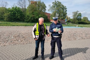 Policjanci ruchu drogowego rozmawiają z grupą motocyklistów i wręczają im szelki odblaskowe