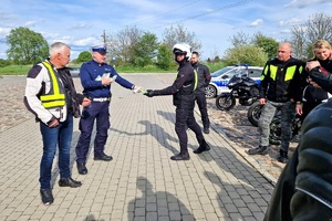 Policjanci ruchu drogowego rozmawiają z grupą motocyklistów i wręczają im szelki odblaskowe