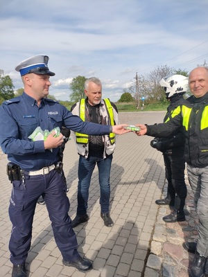 Policjanci ruchu drogowego rozmawiają z grupą motocyklistów i wręczają im szelki odblaskowe
