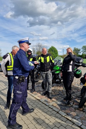 Policjanci ruchu drogowego rozmawiają z grupą motocyklistów i wręczają im szelki odblaskowe