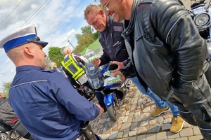 Policjanci ruchu drogowego rozmawiają z grupą motocyklistów i wręczają im szelki odblaskowe