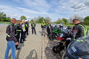 Policjanci ruchu drogowego rozmawiają z grupą motocyklistów i wręczają im szelki odblaskowe