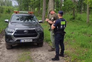 Policjant i strażnik leśny obsługują drona obserwującego teren lasu