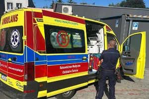 Policjant stoi przy karetce, wewnątrz siedzi poszukiwany