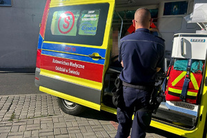 Policjant stoi przy karetce, wewnątrz siedzi poszukiwany