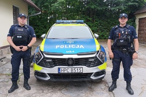 Umundurowani policjanci stoją po bokach radiowozu