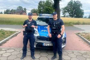 Umundurowani policjanci stoją przed radiowozem