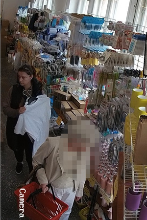Kobieta trzymająca ubrania na wieszakach, która okradła inną klientkę