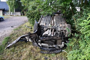 Samochód osobowy po dachowaniu i policjant wykonujący czynności na miejscu zdarzenia