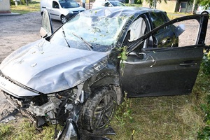 Samochód osobowy po dachowaniu i policjant wykonujący czynności na miejscu zdarzenia