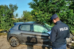 Samochód osobowy po dachowaniu i policjant wykonujący czynności na miejscu zdarzenia