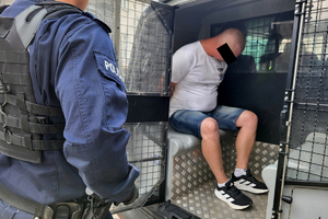 Zatrzymany siedzi w radiowozie, obok stoi policjant