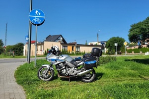 Policjant mierzy prędkość pojazdów, w pobliżu stoi policyjny motocykl