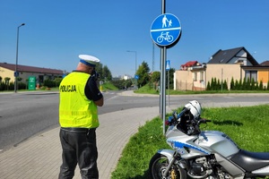 Policjant mierzy prędkość pojazdów, w pobliżu stoi policyjny motocykl