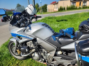 Policjant mierzy prędkość pojazdów, w pobliżu stoi policyjny motocykl