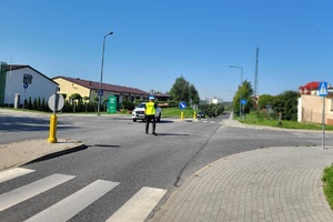 Policjant mierzy prędkość pojazdów, w pobliżu stoi policyjny motocykl