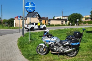 Policjant mierzy prędkość pojazdów, w pobliżu stoi policyjny motocykl