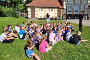 Policjantki rozmawiają z grupą dzieci przed budynkiem szkoły