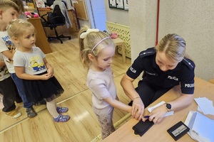 Policjantka prowadzi zajęcia z przedszkolakami, rozdaje odblaski i kolorowanki