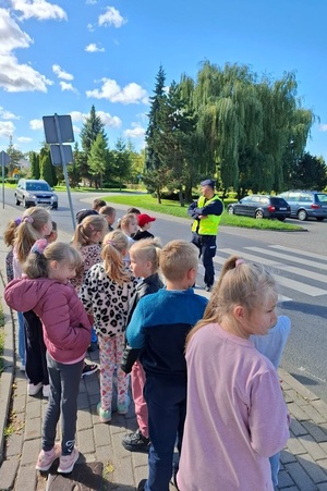 Dzielnicowy prowadzi z uczniami lekcję bezpieczeństwa a następnie ćwiczenia praktyczne na drodze