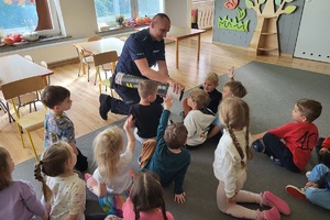 Mundurowy tłumaczy dzieciom zasadę działania odblasków przy użyciu magicznej tuby