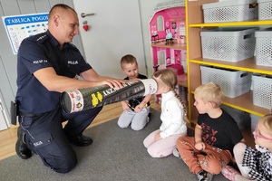 Mundurowy tłumaczy dzieciom zasadę działania odblasków przy użyciu magicznej tuby